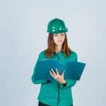 Builder Woman In Green Helmet, Shirt Looking At Folder And Looking Wistful , Front View