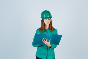 builder woman in green helmet, shirt looking at folder and looking wistful , front view